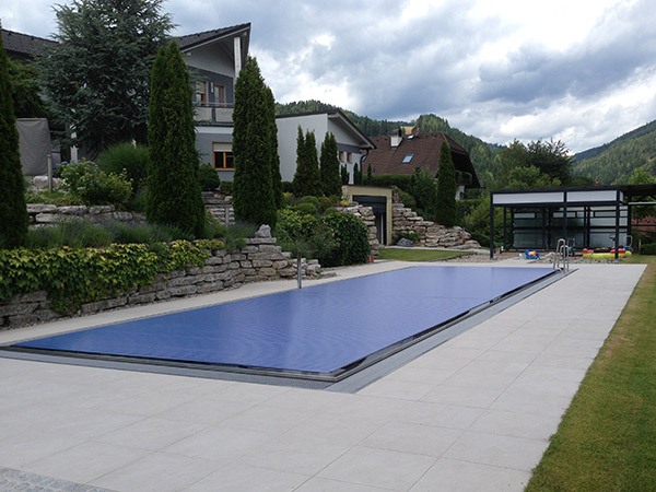 Außenanlage mit großen rechteckigen Pool und Steinplatten rundherum gelegt, im hinteren Bereich eine moderne Pergula.